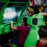 anonymous boy playing car racing simulator near mother and sibling