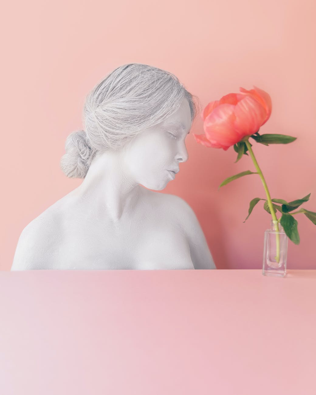pink flower in vase near female bust